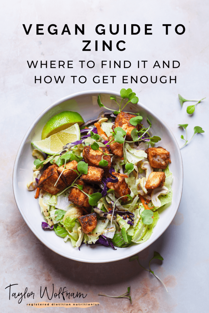 A bowl of marinated, cooked tofu over lettuce and topped with cashews, carrots, cabbage, microgreens, with a couple lime wedges.