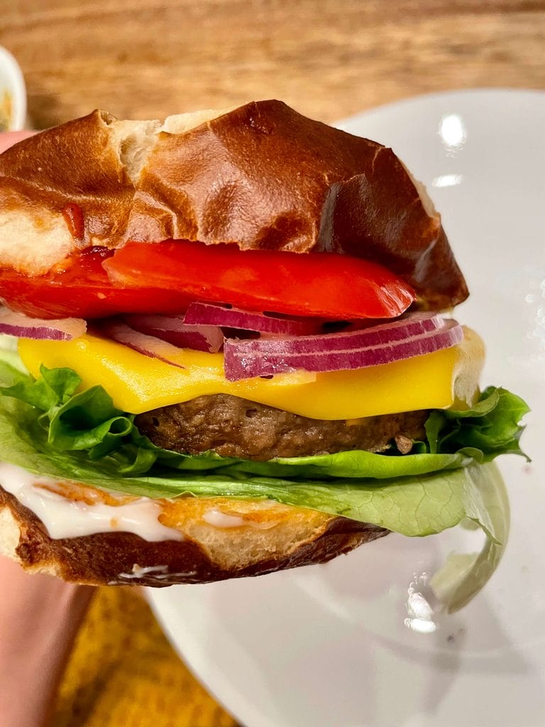 A vegan cheeseburger on a pretzel bun with lettuce, red onion, tomato and mayo. 