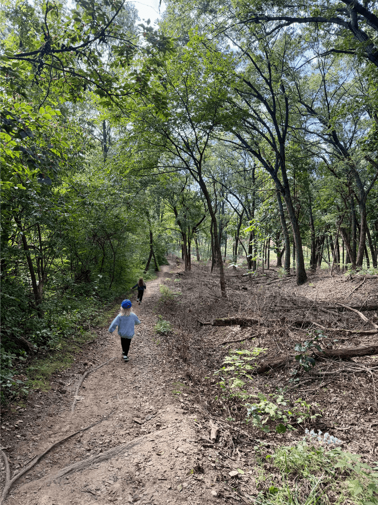 Two little kids running down a dirt trail through a forest